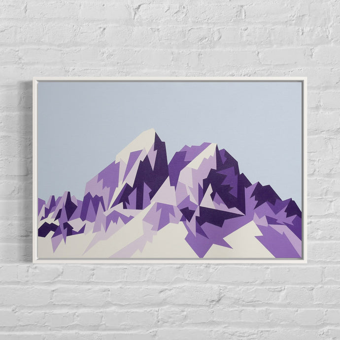 Framed artwork of a mountain range with purple and beige colors on a white brick wall.